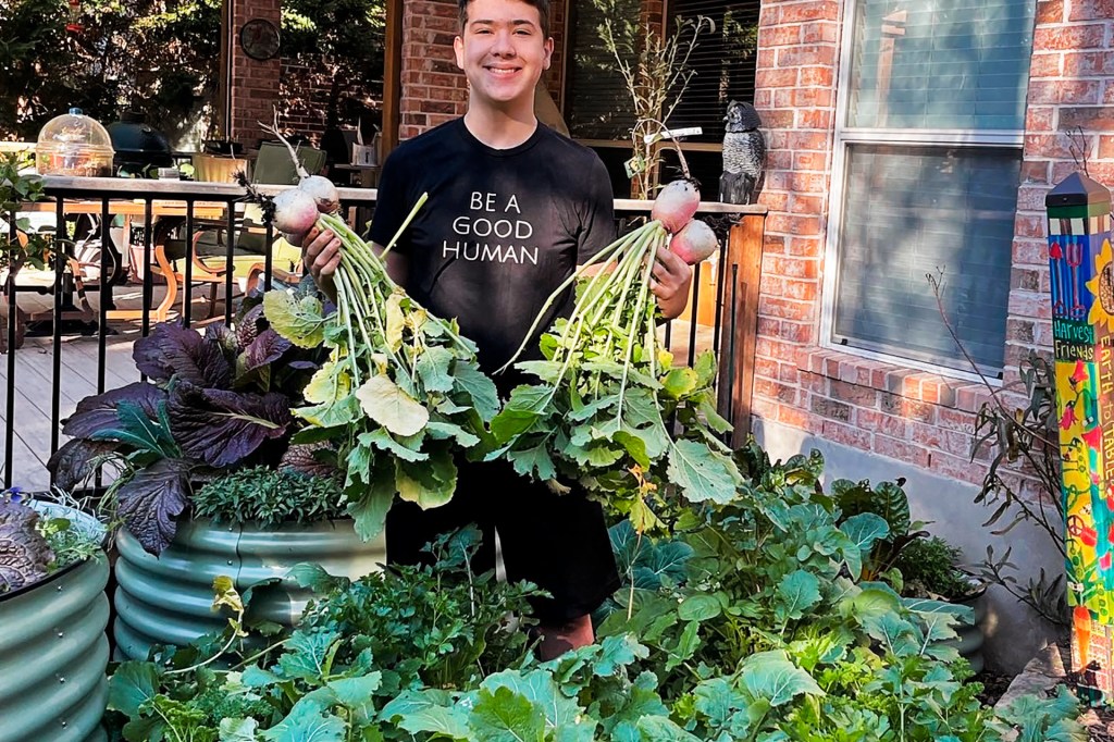 boy holding vegetables on either hand surrounded by garden of vegetables