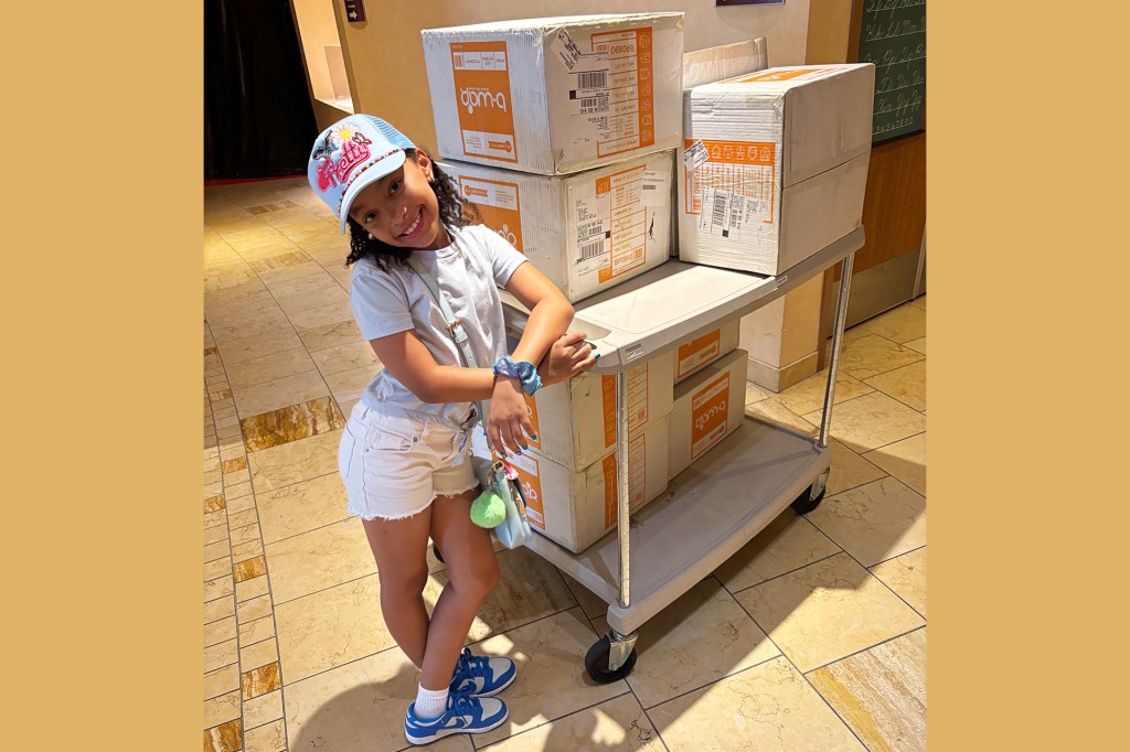 A smiling girl leans against a cart loaded with cardboard boxes.