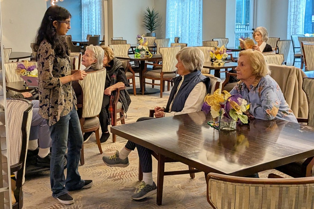 A teenage girl speaking to a group of seniors in a meeting room.