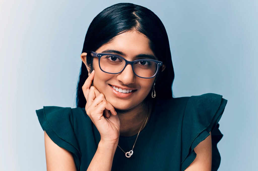 A smiling teenage girl wearing glasses in front of a light blue background