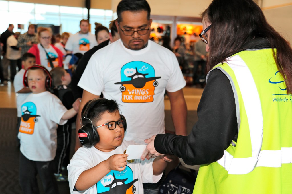 A boy wearing headphones hands his ticket to an airline worker in an airport.