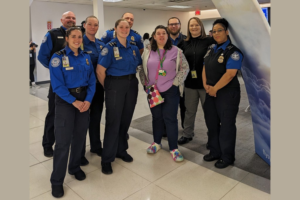 A woman stands with a group of TSA workers in an airport