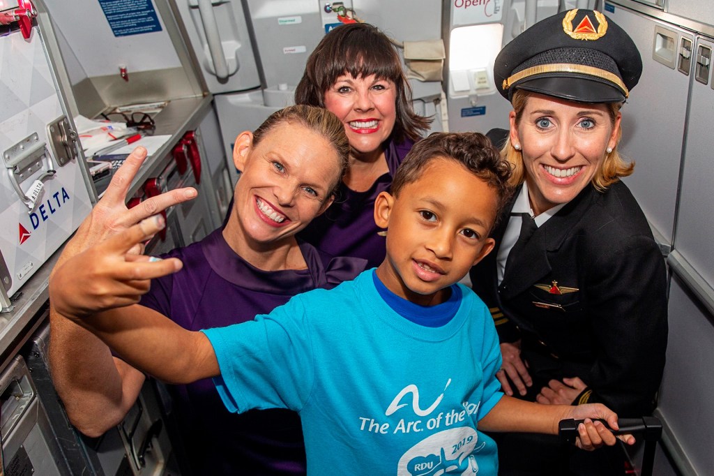 A stands with airline crew near storage cabinets in a plane