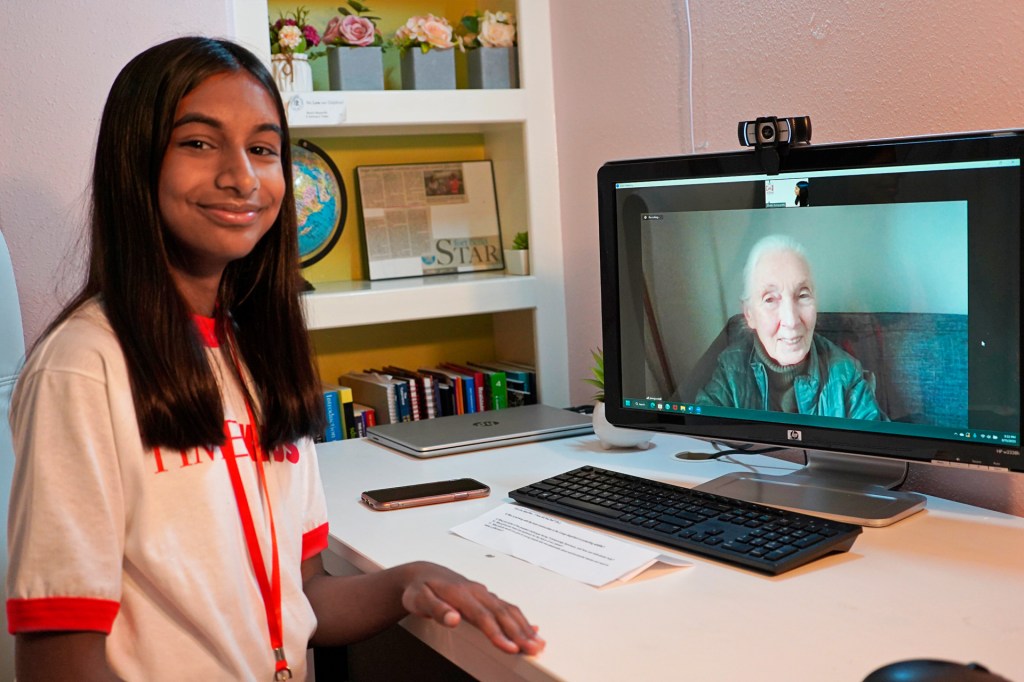 A smiling girl looking at the camera. On her desk, a woman on a video conference looks into the camera, smiling.
