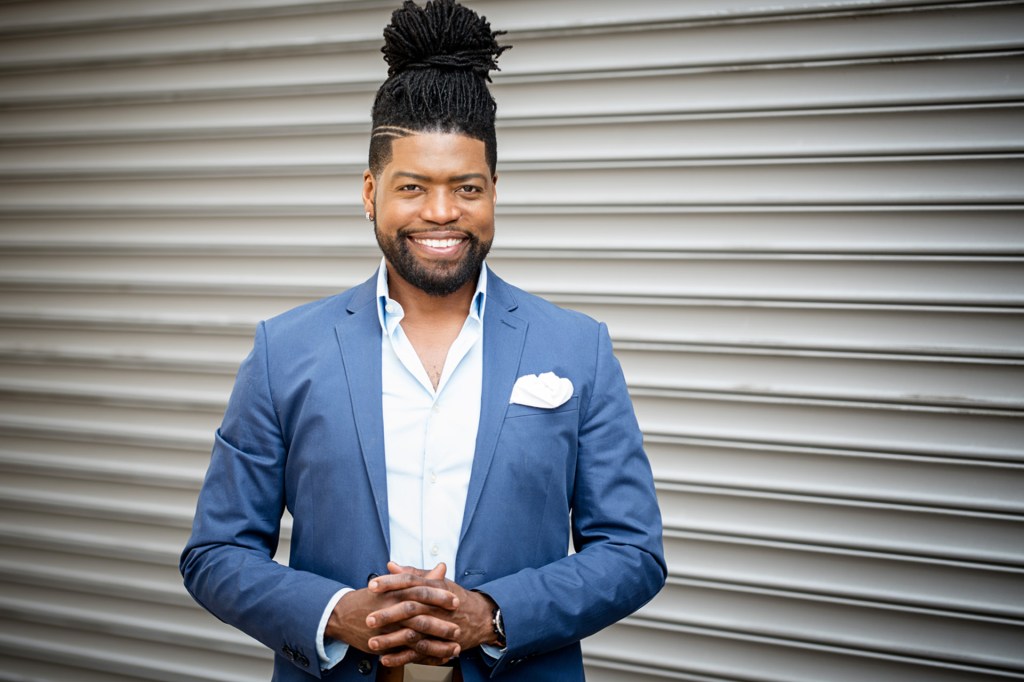 Portrait of a smiling man in a blue suit jacket and white shirt standing in front of a metal wall.