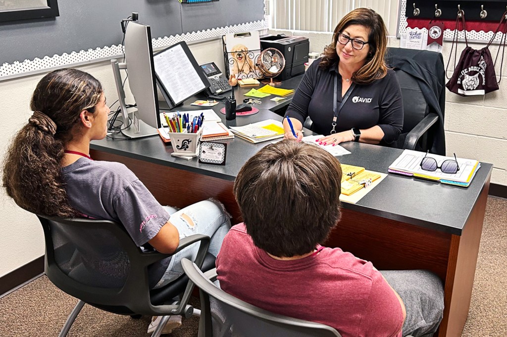 School counselor sits at her desk talking with two students seated across from her.