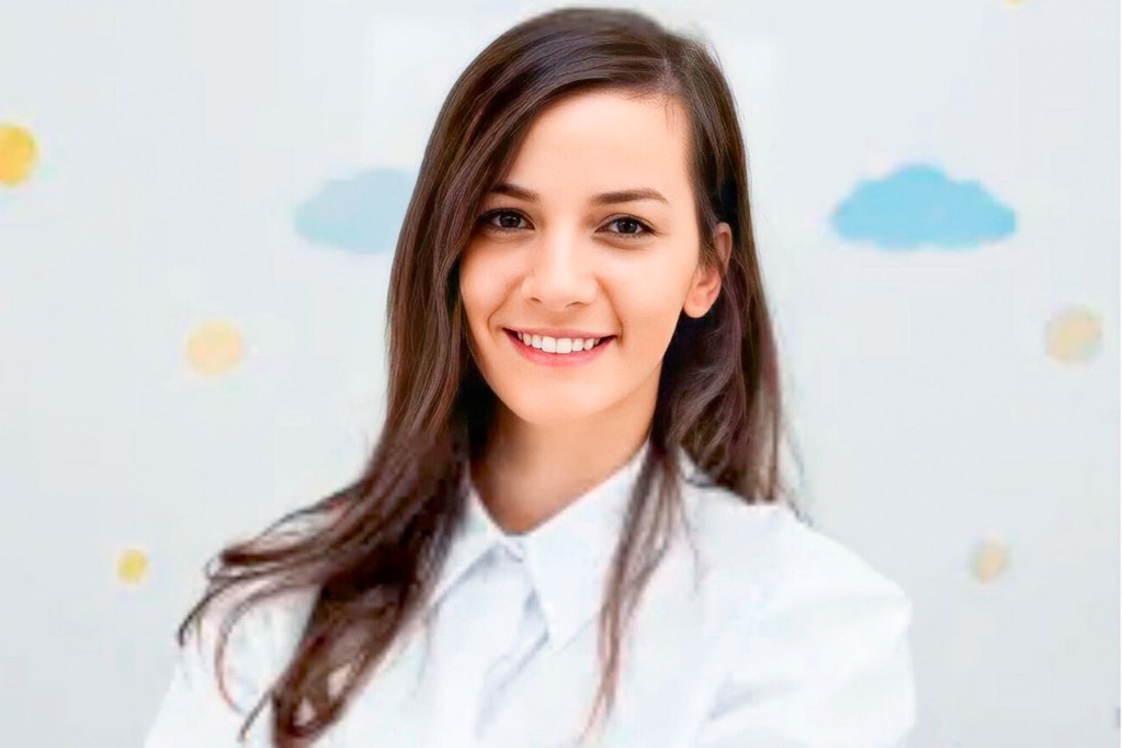Smiling woman in a white blouse stands in front of a light background with colorful circles and clouds.