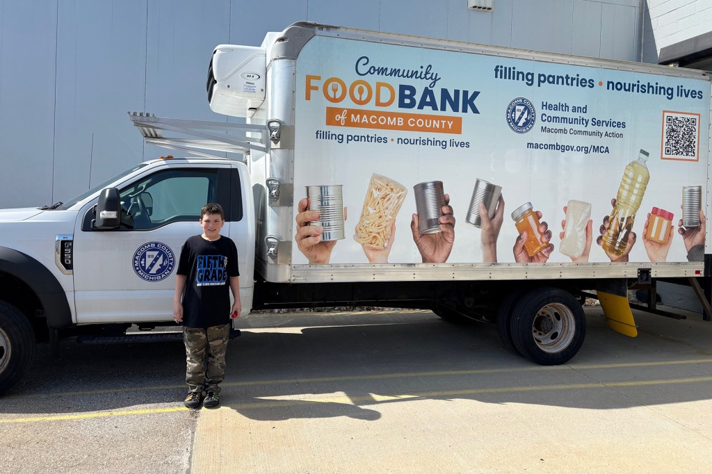 Boy in a black t-shirt stands in front of a truck labeled “Community Food Bank of Macomb County.”