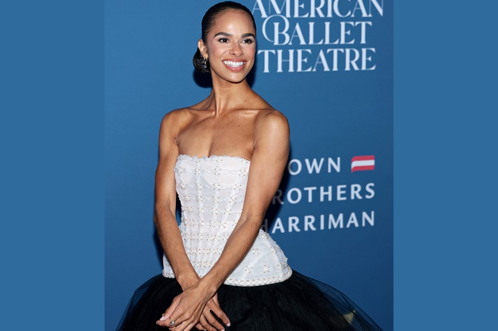 Smiling woman in a strapless white top and black skirt poses in front of a blue American Ballet Theatre backdrop.