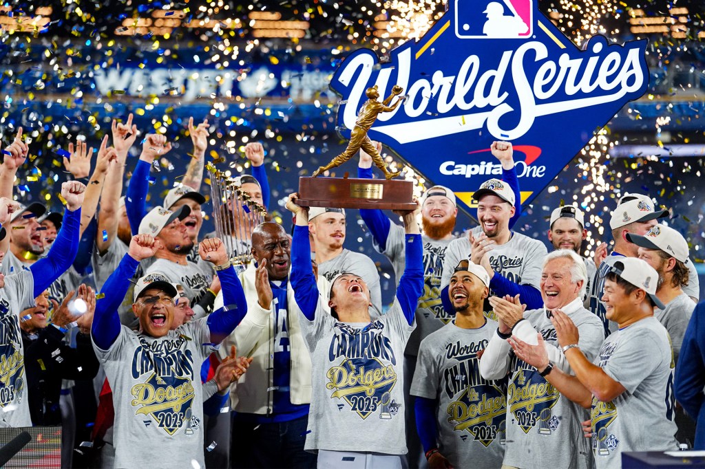 Baseball players wearing “Dodgers 2025 World Champions” shirts cheer and lift a trophy during a World Series celebration.